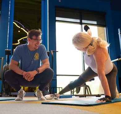 Personal trainer coaching a woman through a stretching exercise on a mat in a bright gym setting at Legacy Personal Training.