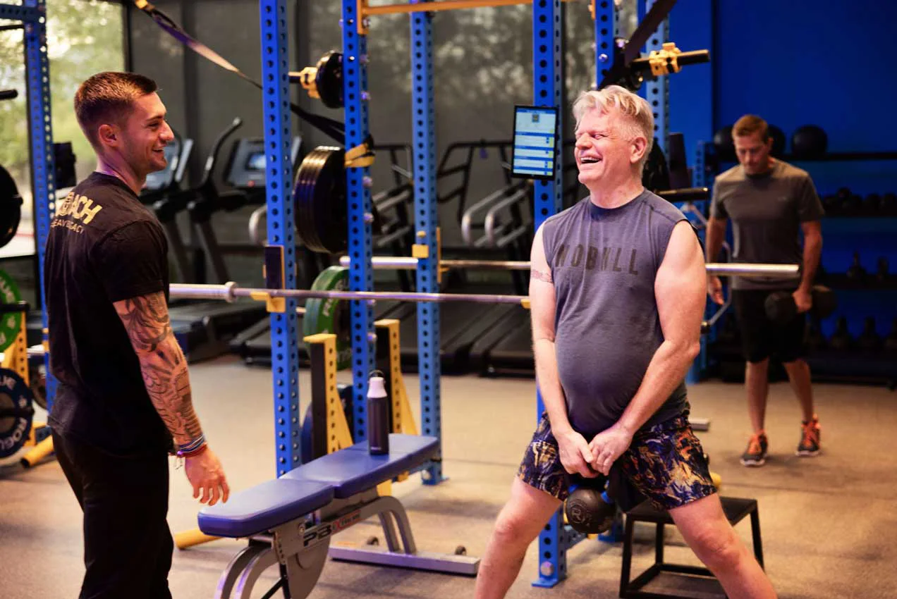 Personal trainer coaching a man through a strength exercise in a bright gym setting at Legacy Personal Training.